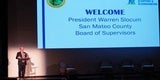 Presenter standing next to a welcome slide projected on screen