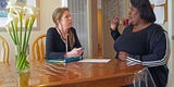 two women talking while seated at table. 