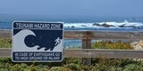 tsunami hazard zone sign on fence in front of ocean cliffs