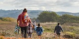Woman in red jacket with childs backpack walks behind three children on coastal bluff
