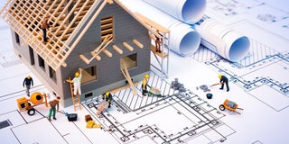 A minature house being constructed on top of a set of plans.