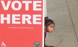 Little girl underneath "Vote Here" sign