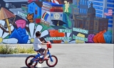 child on bike infront of mural