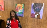 Artist Angela Homes stands smiling in front of her floral artwork