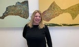 Artist Carol Sconzert in a black shirt stands in front of her abstract paintings