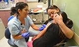 Medical technician in scrubs smiling warmly and giving a shot to a girl in her mom's arms