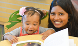 Woman of color smiling with small child looking at a book