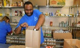 Two Samaritan House Food Pantry volunteers in blue tshirts pack food in grocery bags. 