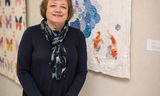 Woman stands smiling next to her quilt 