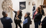 A group of people listen to an artist explain her fabric artwork