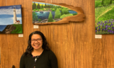 Smiling woman standing under a woodcut painting of a river