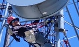 View of a worker on a radio tower near a circular microwave antenna