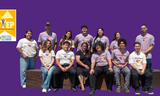A diverse group of 13 people smiling and posing together against a solid purple background. In the top left corner is the yellow logo for STEP (Supported Training & Employment Program).