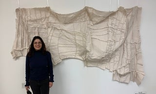 Woman stands in front of her massive intricate and textured artwork