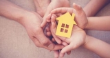 Adult and child cupped hands holding a cutout of a yellow house