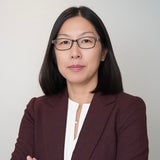 woman with brown hair to shoulders, wearing glasses and with arms crossed