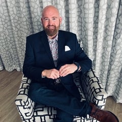 person in suit, sitting in chair with one leg crossed over the over