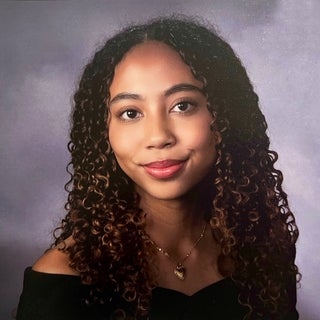 Teen girl with long curly brown hair and is smiling into the camera