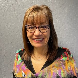 woman with shoulder length brown hair, glasses, smiling toward the camera
