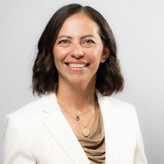 woman with brown hair and light eyes wearing a cream jacket and tan shirt