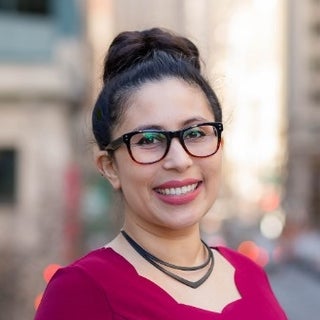 woman with brown hair in a bun, dark framed glasses, wearing red